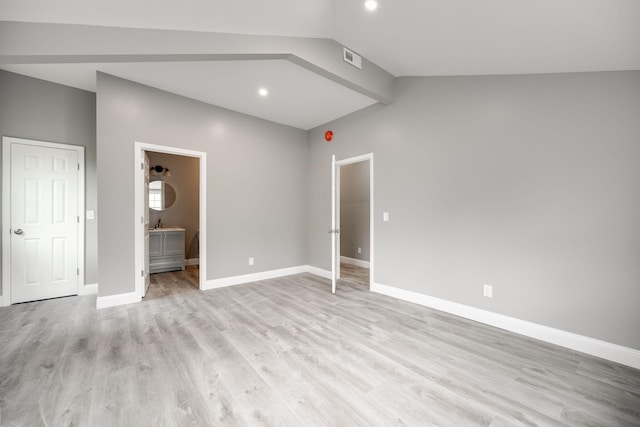 unfurnished bedroom featuring vaulted ceiling, light wood-type flooring, and ensuite bath