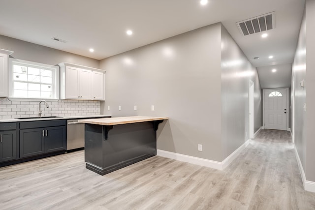 kitchen featuring dishwasher, a kitchen breakfast bar, sink, light hardwood / wood-style flooring, and white cabinetry