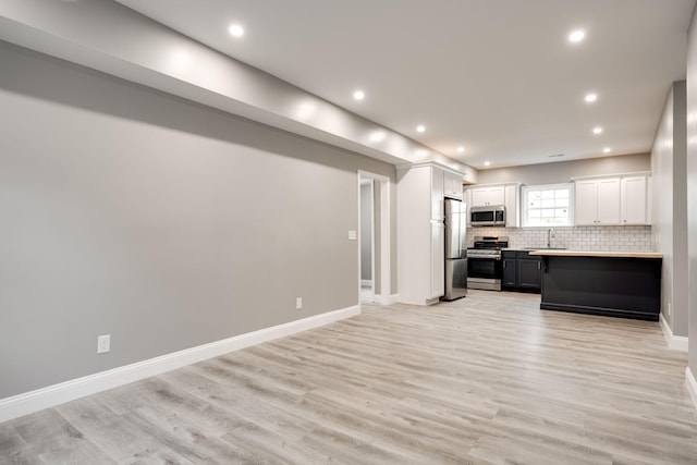 kitchen with appliances with stainless steel finishes, light wood-type flooring, tasteful backsplash, sink, and white cabinets