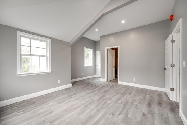 spare room featuring a healthy amount of sunlight, light wood-type flooring, and vaulted ceiling