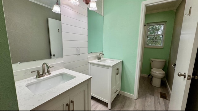 bathroom featuring toilet, vanity, wood-type flooring, and ornamental molding