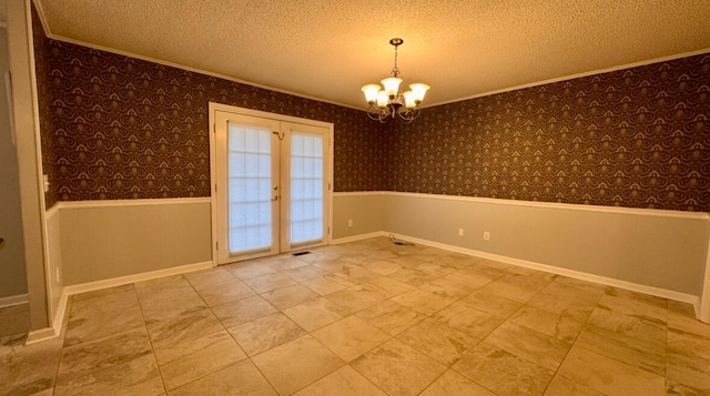 empty room with a textured ceiling, a chandelier, crown molding, and french doors