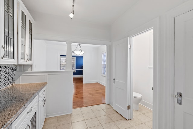 kitchen with light stone countertops, white cabinetry, light hardwood / wood-style floors, decorative light fixtures, and decorative backsplash