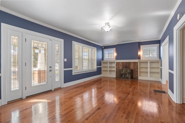 interior space with wood-type flooring, a brick fireplace, a wealth of natural light, and ornamental molding