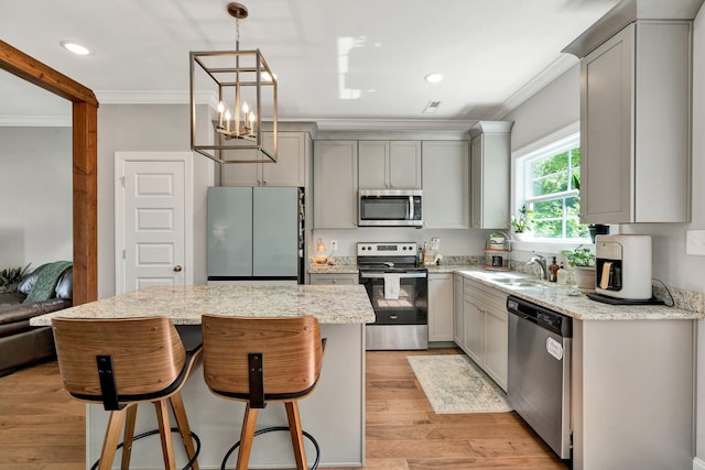 kitchen with appliances with stainless steel finishes, ornamental molding, gray cabinets, a sink, and a kitchen island