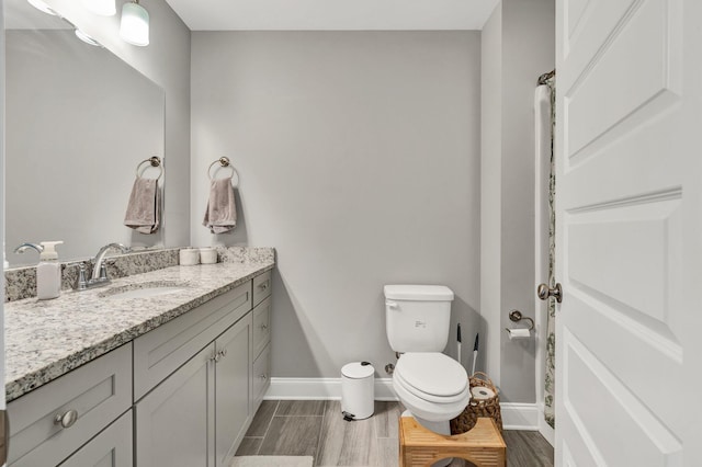 bathroom with baseboards, toilet, vanity, and wood tiled floors