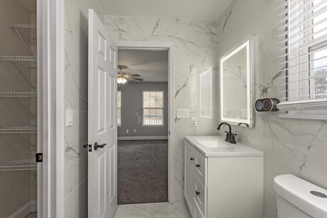 half bathroom with a ceiling fan, toilet, marble finish floor, and vanity
