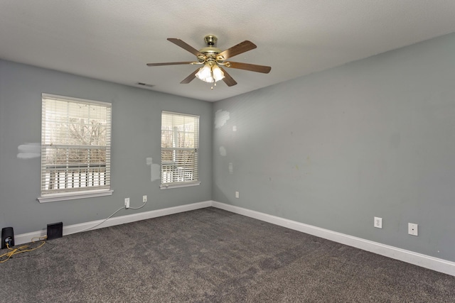 unfurnished room with visible vents, dark carpet, a ceiling fan, and baseboards