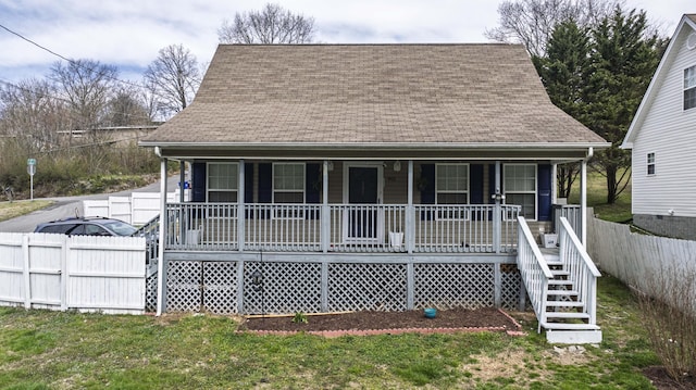 view of front of home with a front lawn, fence, covered porch, and roof with shingles