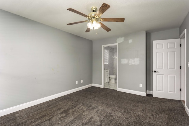 unfurnished bedroom with a ceiling fan, baseboards, dark colored carpet, and ensuite bathroom