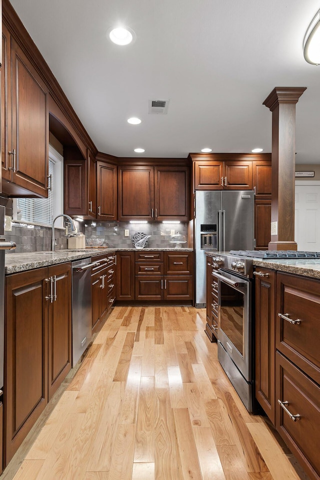 kitchen featuring tasteful backsplash, light stone counters, decorative columns, stainless steel appliances, and light hardwood / wood-style floors