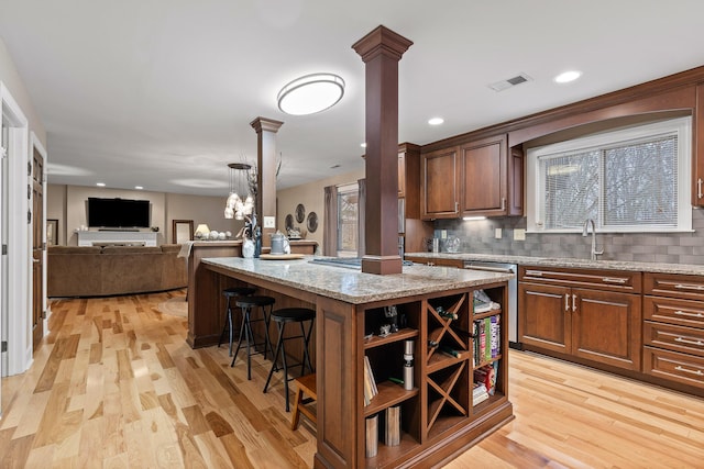 kitchen with a center island, light wood-type flooring, light stone counters, a kitchen bar, and decorative columns