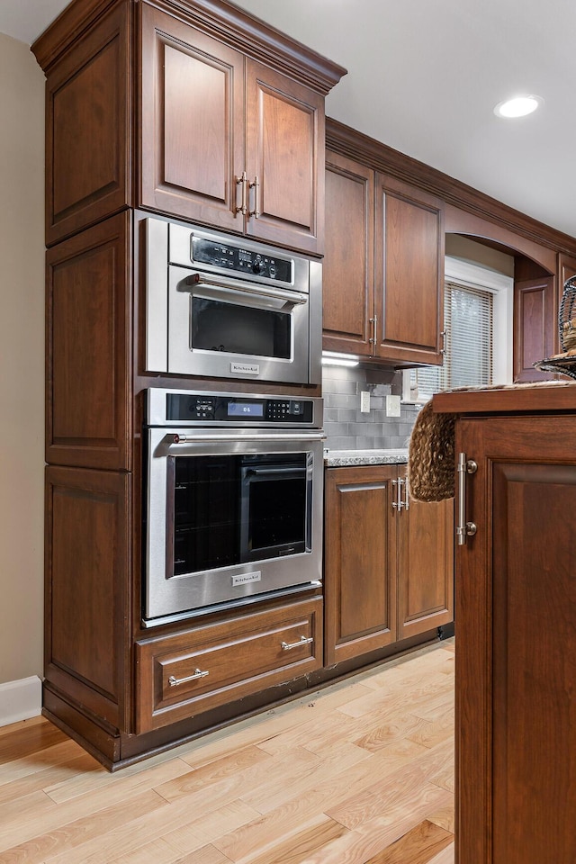 kitchen featuring double oven, backsplash, light stone countertops, and light wood-type flooring