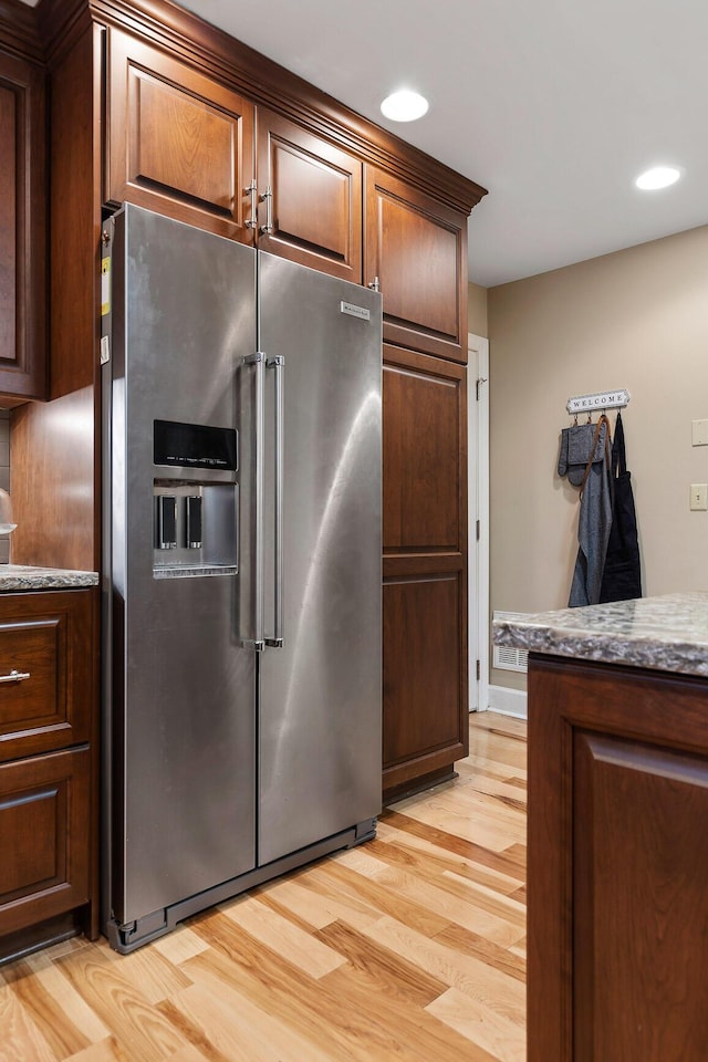 kitchen with high end refrigerator, light hardwood / wood-style flooring, and dark stone counters