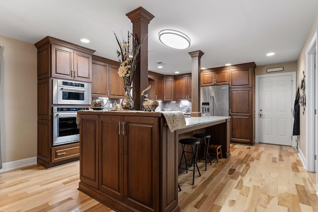 kitchen featuring a center island, light stone countertops, ornate columns, a kitchen bar, and stainless steel appliances