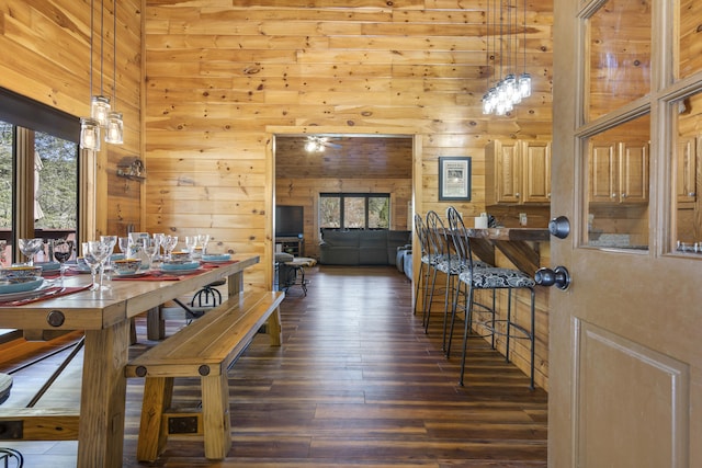 dining area with a high ceiling, wood walls, plenty of natural light, and dark wood-type flooring