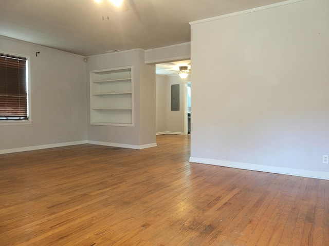 spare room with ceiling fan, electric panel, ornamental molding, built in shelves, and light wood-type flooring
