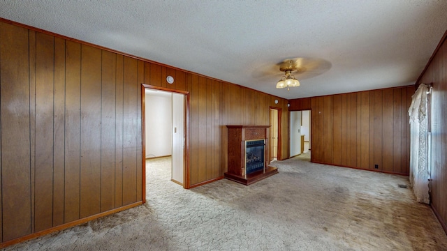 unfurnished living room featuring wooden walls, light carpet, a textured ceiling, and ceiling fan