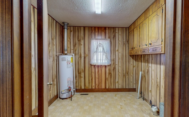 washroom with cabinets, a textured ceiling, water heater, and wood walls