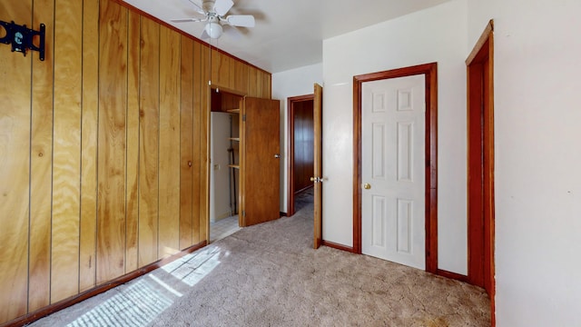 unfurnished bedroom featuring ceiling fan, light carpet, and wood walls