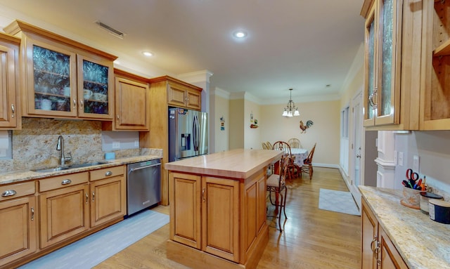 kitchen with a sink, stainless steel appliances, light wood-type flooring, and ornamental molding