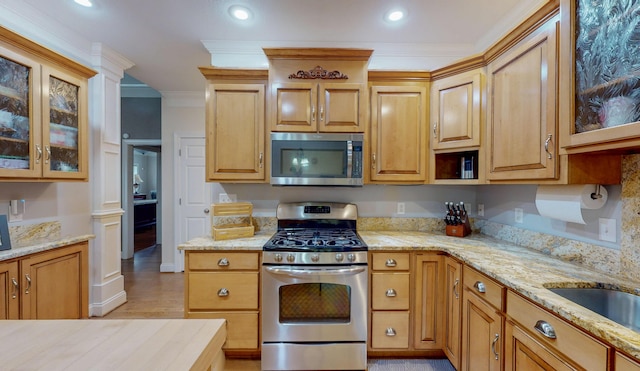 kitchen with glass insert cabinets, light stone countertops, appliances with stainless steel finishes, and ornamental molding