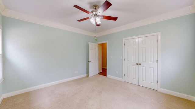 unfurnished bedroom featuring carpet, baseboards, ornamental molding, a closet, and a ceiling fan