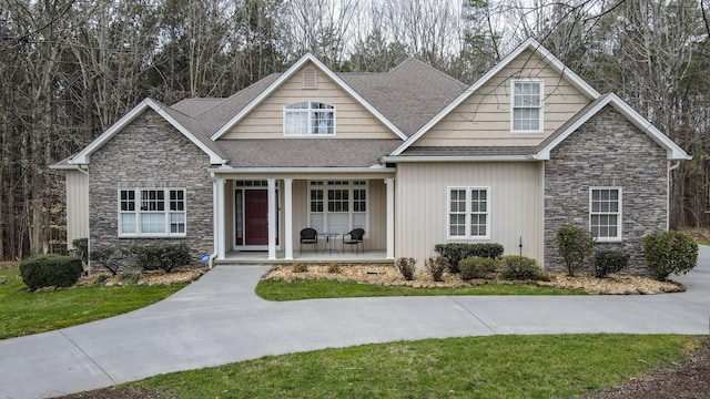 craftsman inspired home featuring stone siding, a porch, a shingled roof, and a front lawn