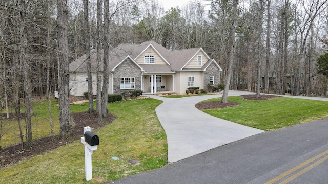 view of front of property featuring a forest view, stone siding, curved driveway, and a front yard