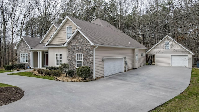 view of front of property featuring a garage, stone siding, an outbuilding, and roof with shingles