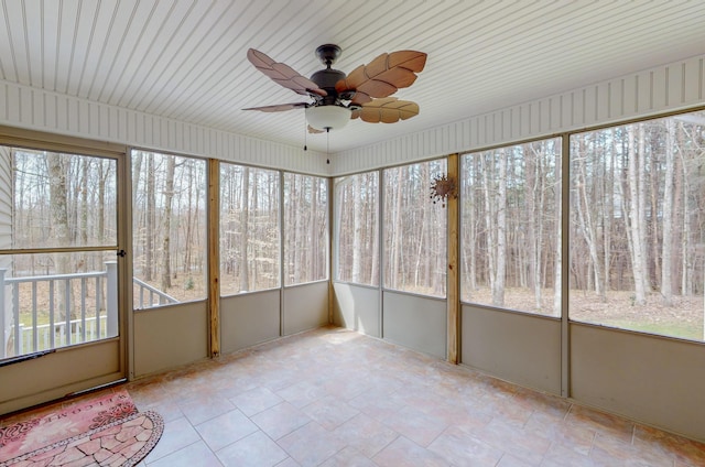 unfurnished sunroom featuring a forest view and ceiling fan