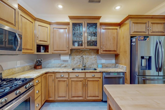 kitchen featuring a sink, light stone counters, appliances with stainless steel finishes, crown molding, and glass insert cabinets