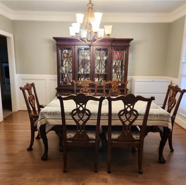 dining area featuring a decorative wall, a wainscoted wall, ornamental molding, wood finished floors, and a notable chandelier