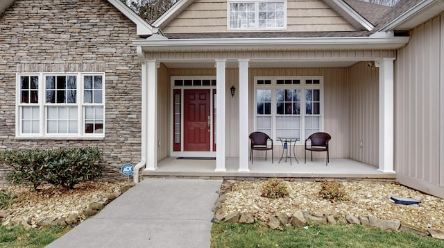 property entrance with stone siding, covered porch, and a shingled roof