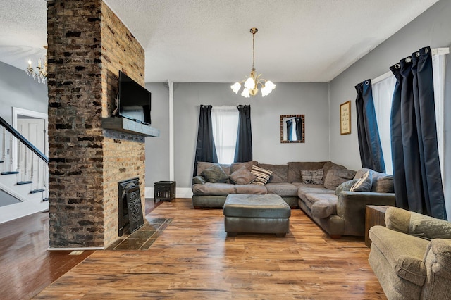 living room featuring a brick fireplace, a textured ceiling, hardwood / wood-style flooring, and a notable chandelier