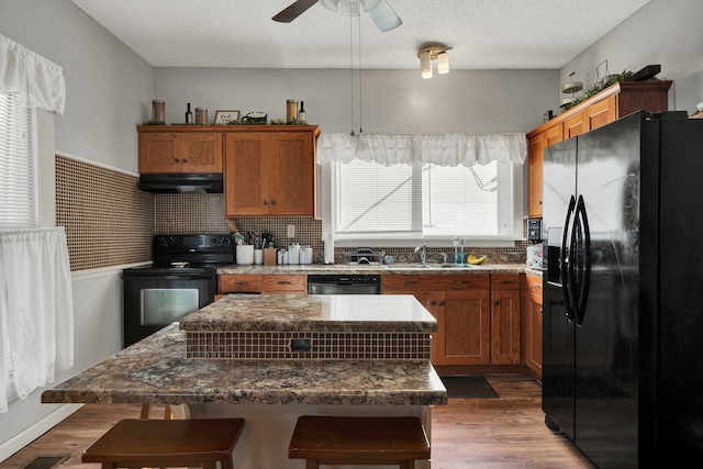 kitchen featuring black appliances, a kitchen island, a kitchen breakfast bar, sink, and hardwood / wood-style flooring