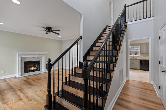 stairs featuring sink, ornamental molding, ceiling fan, a fireplace, and hardwood / wood-style floors