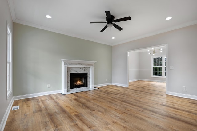 unfurnished living room with ornamental molding, a premium fireplace, ceiling fan, and light wood-type flooring