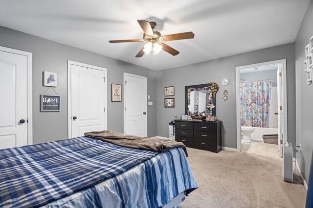 bedroom with ceiling fan, ensuite bath, and light carpet