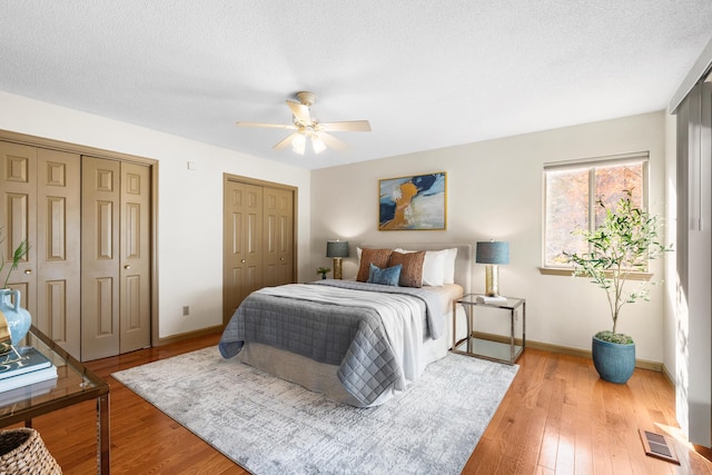 bedroom with a textured ceiling, light wood-type flooring, and multiple closets