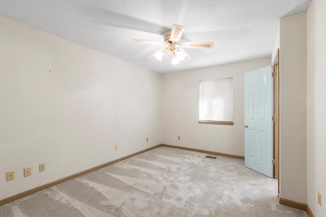 empty room with ceiling fan, light colored carpet, and a textured ceiling