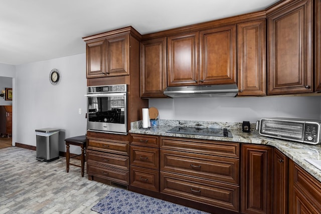 kitchen with light stone counters, baseboards, under cabinet range hood, stainless steel oven, and black electric cooktop