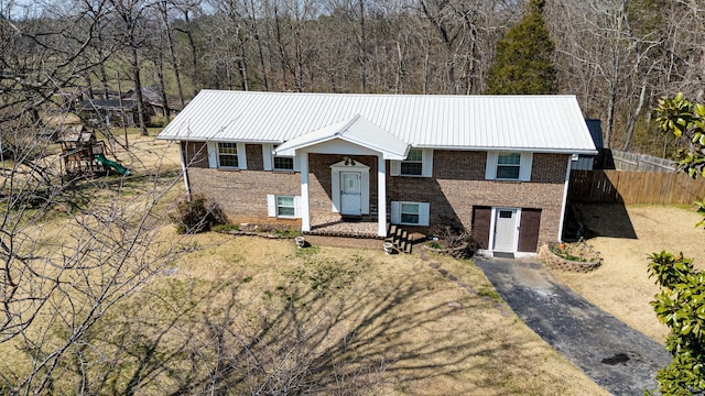 split foyer home featuring brick siding, a playground, fence, metal roof, and driveway