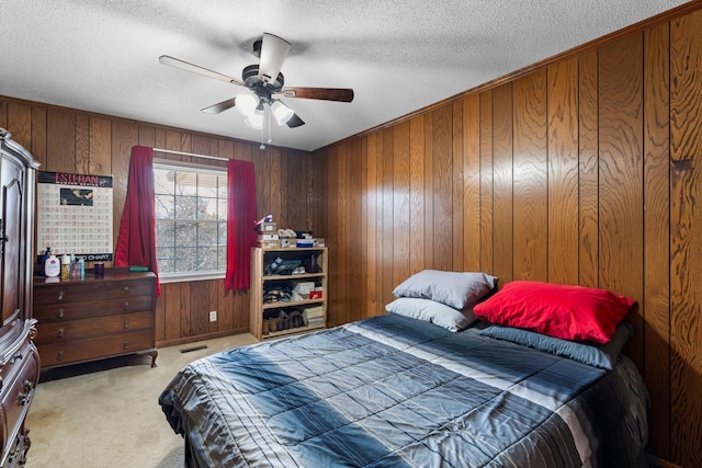 bedroom featuring light carpet, wooden walls, a ceiling fan, and a textured ceiling