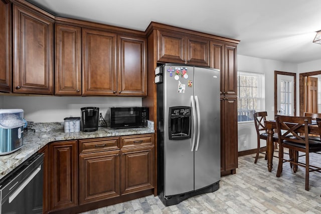 kitchen featuring brick floor, light stone counters, stainless steel refrigerator with ice dispenser, and black microwave