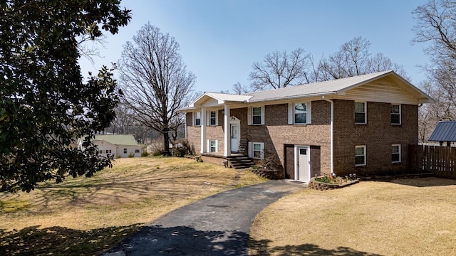 view of front of property featuring brick siding, a front lawn, fence, metal roof, and driveway