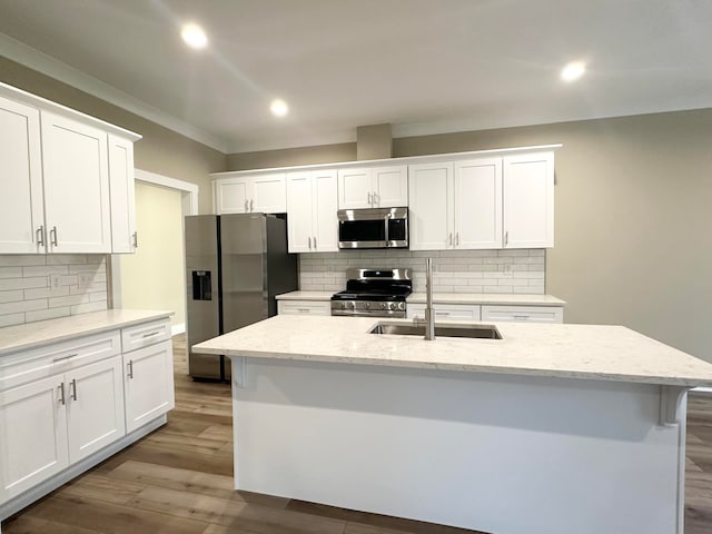 kitchen with light stone countertops, white cabinetry, sink, stainless steel appliances, and an island with sink