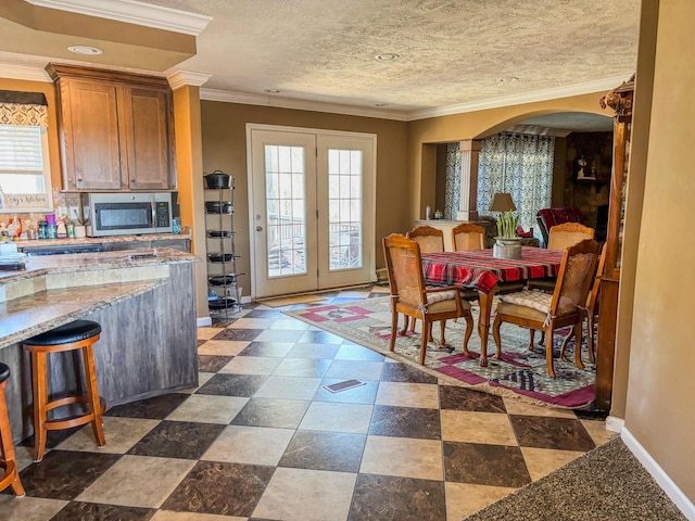 dining space featuring a healthy amount of sunlight, baseboards, ornamental molding, and arched walkways