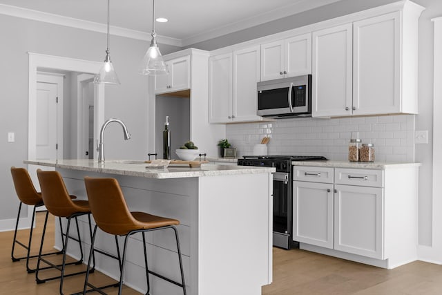 kitchen with stainless steel microwave, stove, white cabinetry, and an island with sink