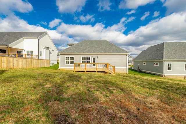 back of property with a yard, a shingled roof, fence, and a wooden deck